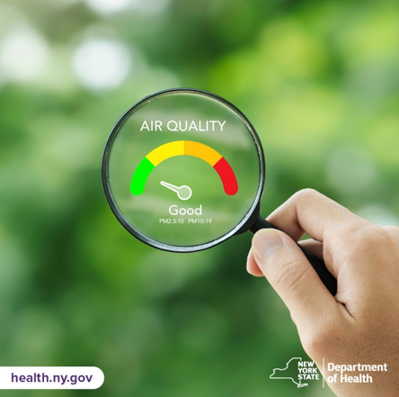A hand holds an air quality measurement device with the indicator showing good air quality.