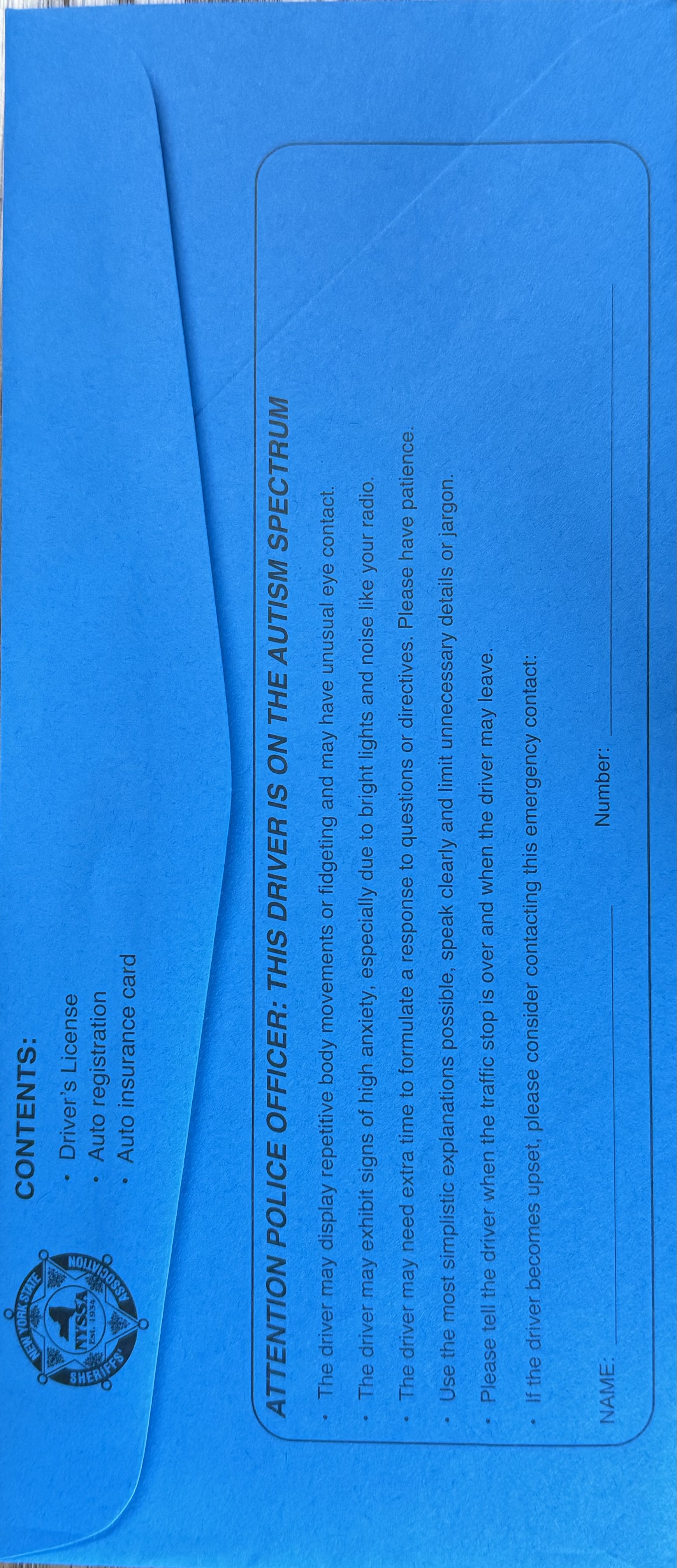 Blue Envelope with text: CONTENTS: • Driver's License • Auto registration • Auto insurance card. ATTENTION POLICE OFFICER: THIS DRIVER IS ON THE AUTISM SPECTRUM • The driver may display repetitive body movements or fidgeting and may have unusual eye contact. • The driver may exhibit signs of high anxiety, especially due to bright lights and noise like your radio. • The driver may need extra time to formulate a response to questions or directives. Please have patience. • Use the most simplistic explanations possible, speak clearly and limit unnecessary details or jargon. • Please tell the driver when the traffic stop is over and when the driver may leave. • If the driver becomes upset, please consider contacting this emergency contact: NAME Number