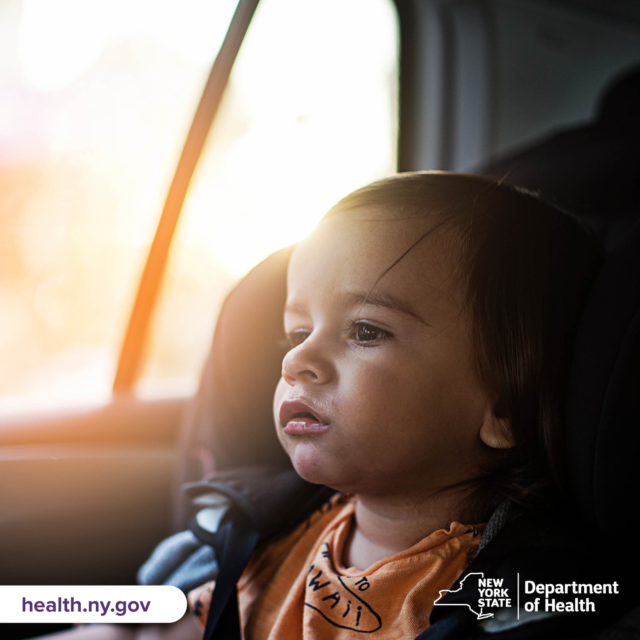 A young child looks out a car window with the sun blaring in.