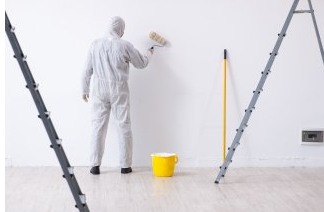 A man in a white painting suit painting a white wall.